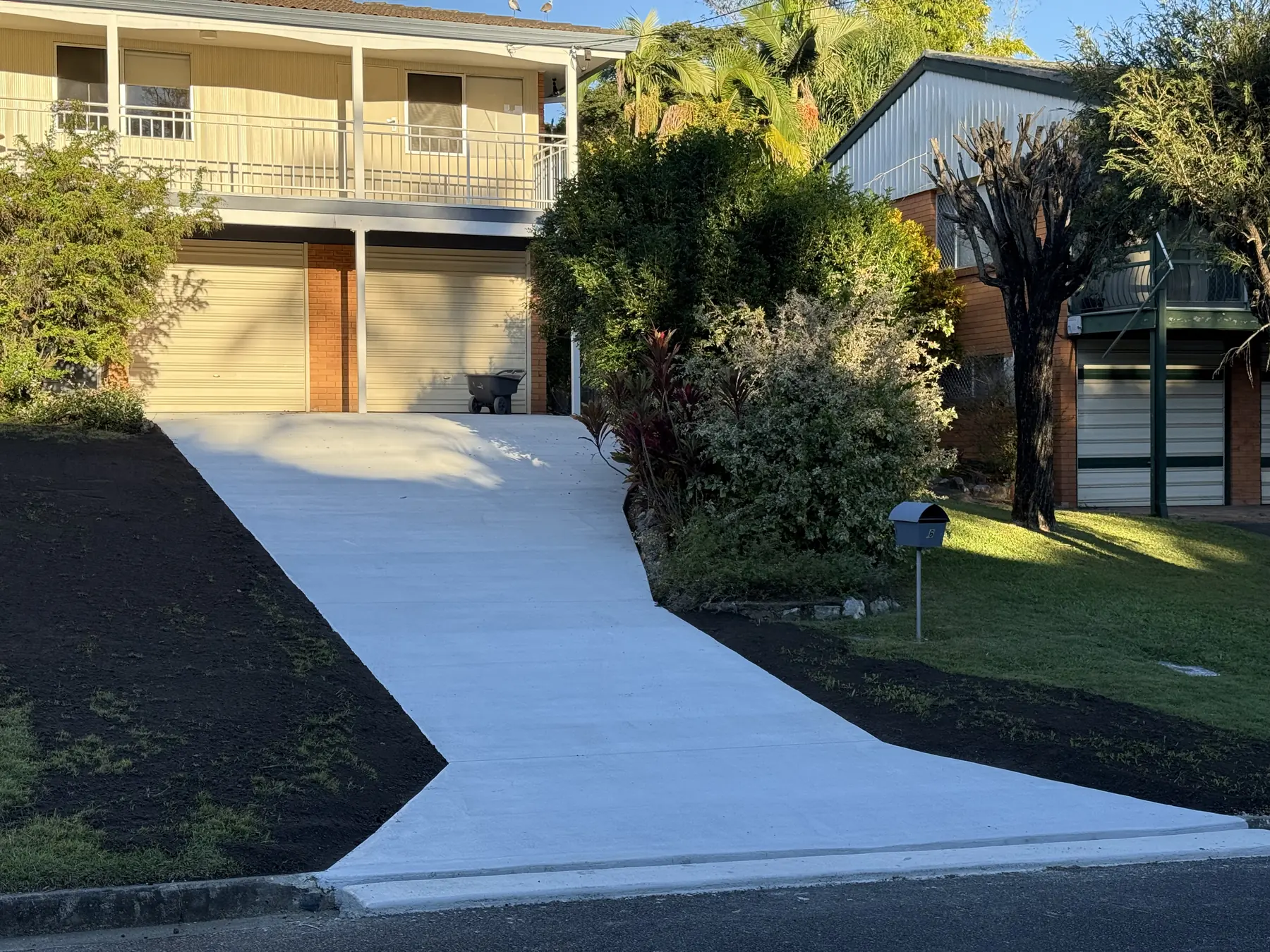 Sloped concrete driveway finished and landscaped up to a high-set home